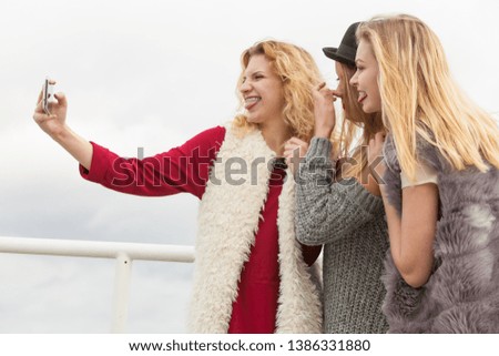 Three females taking selfies, having fun outdoor using smart phone to take photo.