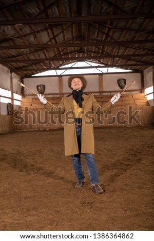 Male cowboy wearing a western hat and trench coat posing in an arena for horses