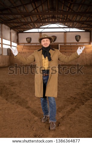 Male cowboy wearing a western hat and trench coat posing in an arena for horses