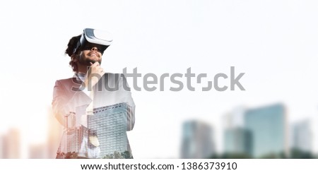 Young handsome businessman in virtual helmet against cityscape background