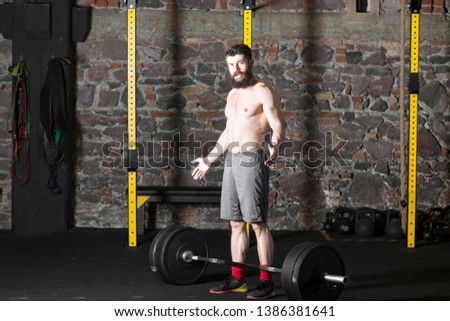 Young beard topless male athlete practicing heavy overhead squat lift at the brick wall background gym. Dark photography concept with copy space text area. 
