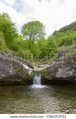 Small mountain waterfall on the rocks covered with moss in the forest in a spring sunny day. 