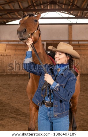 Cowgirl in a cowboy hat and denim suit posing with a horse in the arena