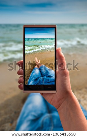 Human take a selfie of legs on a sea beach on smartphone. Travel concept.