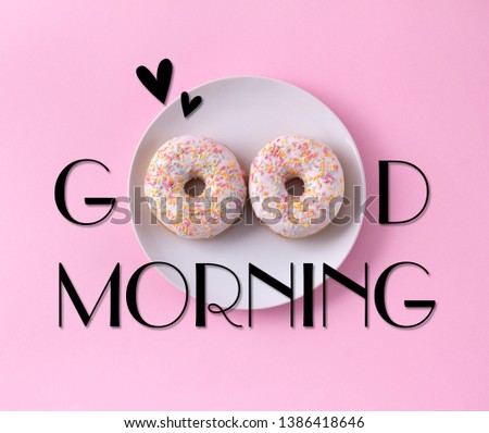 Two donuts on the plate. Good morning greeting written on pink background. Table top view