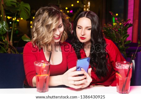 Young women in red clothes drink cocktails and celebrate in a nightclub or bar. Girlfriends take selfies and smile.