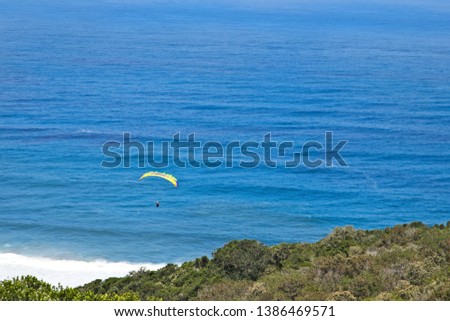An unrecognizable person paragliding over the ocean near Wilderness, South Africa. This is a popular adventure activity in the area. 