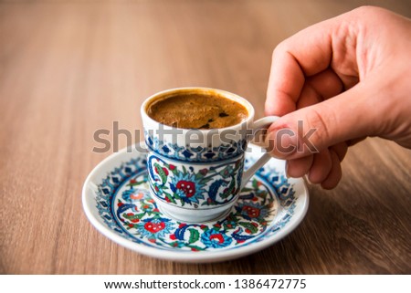 woman hand holding traditional porcelain turkish coffee cup on wooden table