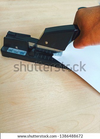 Hand holding a stapler , stapling paper on wooden desk. office equipment stationery stock photo -image