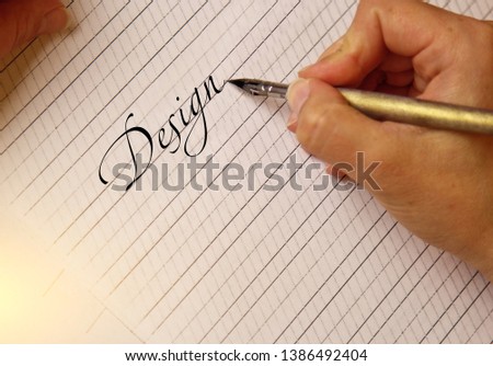 female hand writes by the inky pen the word design on a white paper sheet with stripes. stationery on desk close up top view. spelling lessons and caligraphy exercises. Template, layout, background