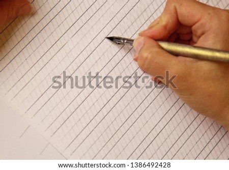 female hand writes with the inky pen on empty white paper sheet with stripes. stationery on desk close up top view. spelling lessons and caligraphy exercises. Template, layout, background.