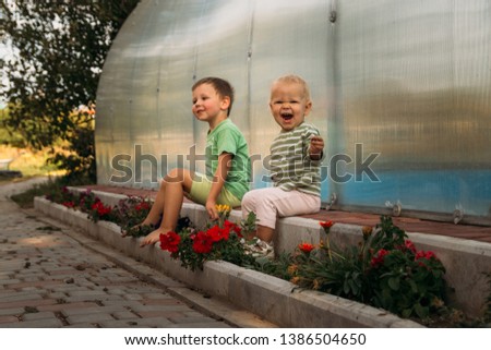 small children, a girl and a boy, sit on a path near a club, barefoot, behind them a covered pool, greenhouse, summer, spring in the village.