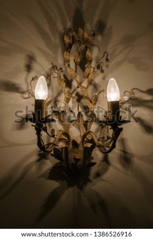 frontal picture of antique chandelier with warm light casting numerous shadows on the wall