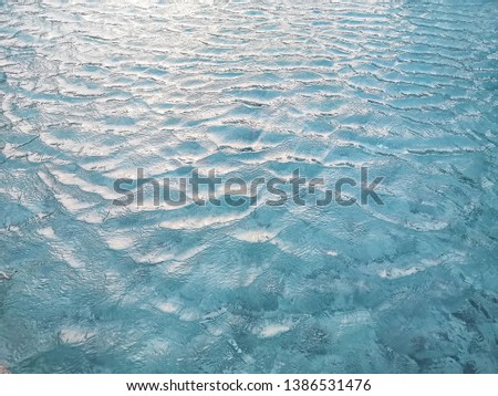 Waving pattern of vivid turquoise blue water in the swimming pool above stone tiles with soft light of reflection of the sunset