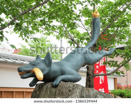 Stone statue of fox in Fushimi Inari Shrine (Japan: Kyoto).
The name of the shrine is written on the red flag.
