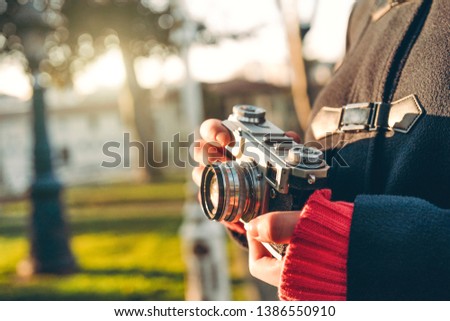 Close up shot of woman's hand holding vintage camera in forest at sunny weather.