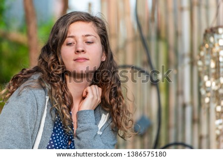 Young woman face closeup looking away in zen bamboo garden with shiny decorations wind chimes sitting