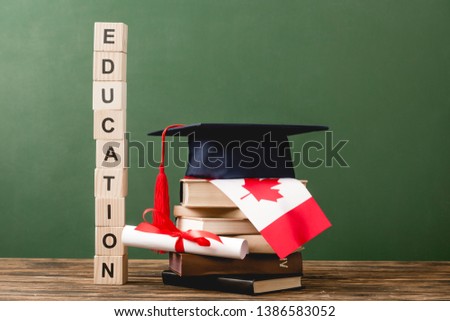 wooden blocks with letters, diploma, books, academic cap and canadian flag on wooden surface isolated on green
