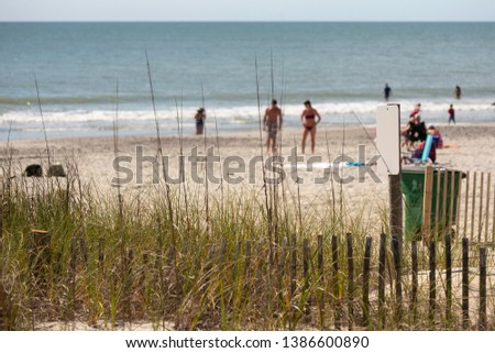 Defocused view of a sparsely populated beach with sand dune fencing in the foreground