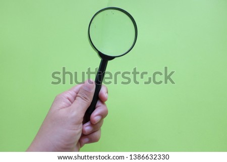 Hand holding a magnifying glass on a green paper background