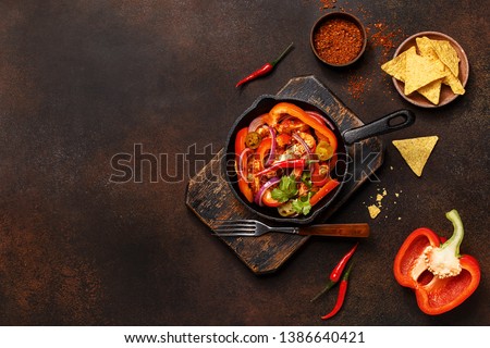 Traditional mexican dish fajitas in cast iron pan on vintage wooden board with nachos and vegetables over dark concrete background. Flat lay, overhead view, copy space
