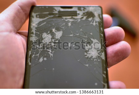 Close-up with selective focus on the shattered screen of a smartphone. In the background, a hammer is blurred.