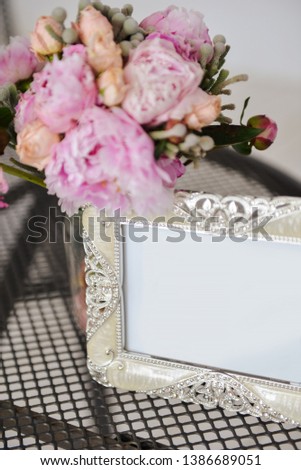 silver frame for a photo is on the table next to a bouquet of pink flowers, soft focus