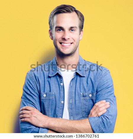 Male portrait. Young happy man with smiling face. Male model in crossed arms pose. Yellow background. Guy in casual fashion clothing, studio photo. Square composition picture.