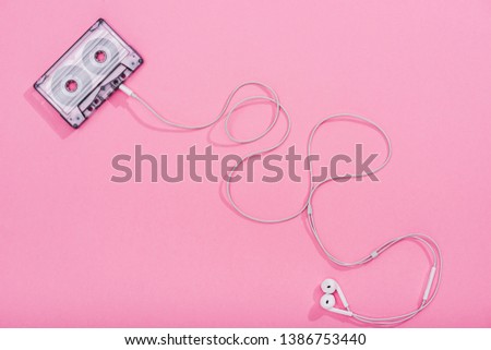 top view of vintage audio cassette with earphones on pink, music concept