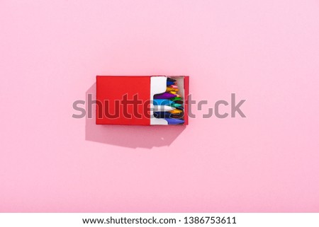 top view of multicolored crayons in red cigarette pack on pink with copy space, smoking concept