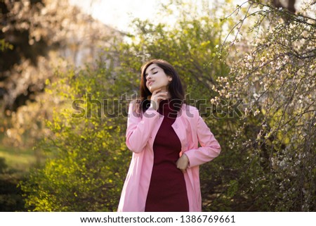 beautiful armenian girl in pink coat laughs at sunset and looks away in city park