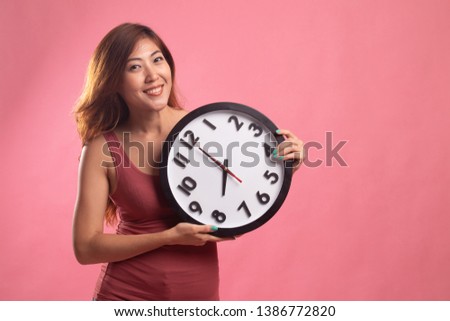 Young Asian woman with a clock on pink background