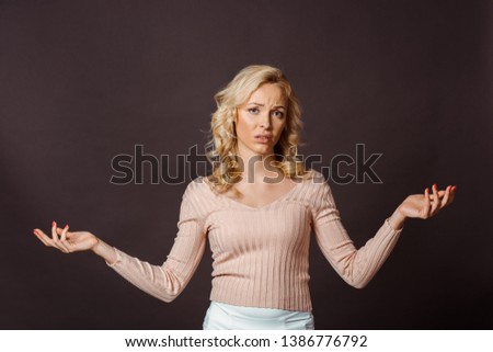 beautiful blonde woman showing shrug gesture isolated on black 