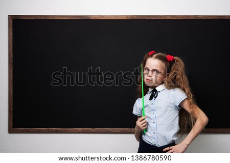 A girl schoolgirl is standing at the school board and holding a pointer.