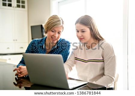 A mother using a laptop in kitchen with teenager Royalty-Free Stock Photo #1386781844