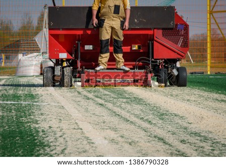 A worker using a special technique pours quartz sand onto an artificial surface. Construction of a football field.
