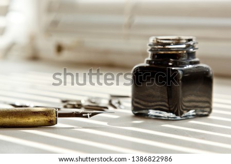 Inkpot with metal tips for the ink pen on a white background in solar rays. stationery on white desk close up top view. spelling lessons and caligraphy exercises. Template, layout, background. Royalty-Free Stock Photo #1386822986