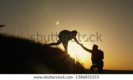 woman traveler stretches hand to man climbing to the top of a hill. travelers climb the cliff holding hands. teamwork of business people. Happy family on vacation. tourists hug on top of mountain