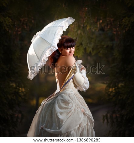 Beautiful woman in vintage dress with a white umbrella on the background of greenery. Selective focus. Gallant century.