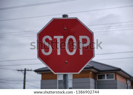 Red stop sign with cloudy sky, power lines and modern house in background in Melbourne, Australia