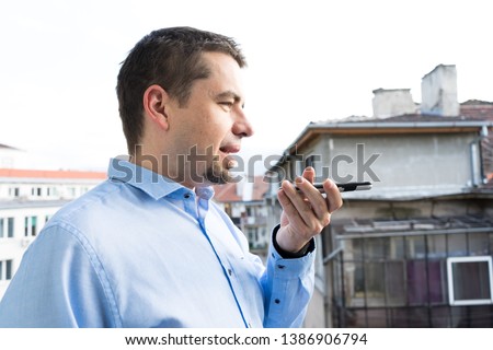 Young Business man with blue shirt using voice recognition in smart phone in the balcony of Bulgaria
