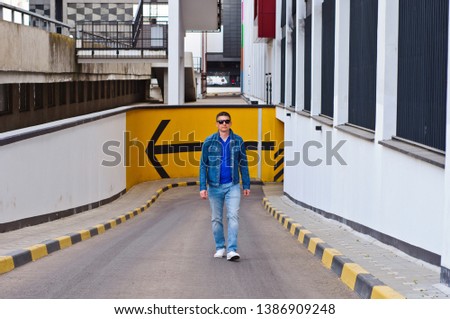 People and modern urban lifestyle concept. Handsome tattooed young guy wearing trendy black clothing sitting on concrete stairs against office building background and waiting for his girlfriend 