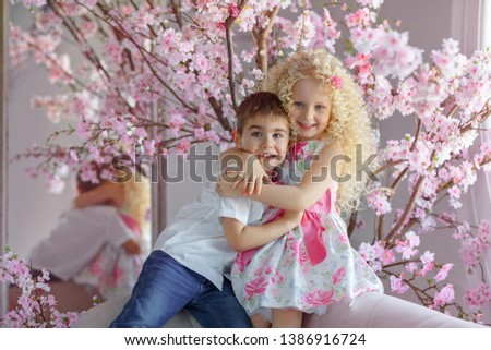 Adorable cute little boy and girl of the blonde are hugging, against the background of pink flowers. Portrait, studio