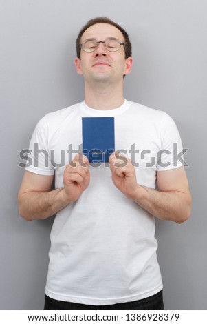 European man with a passport in his hands, wearing glasses, in a white T-shirt, a citizen of the country with a passport, studio photo with a man