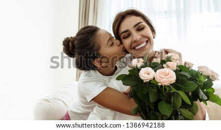 Family. Love. Holiday. Mom and daughter. Girl is giving a bouquet for her mother and kissing her, woman is smiling; at home
