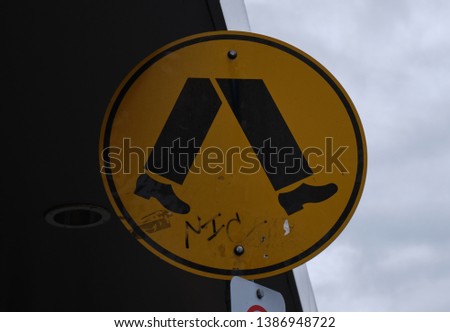Crossing sign, crosswalk sign, pedestrian sign, yellow with black legs walking, cloudy sky in background in Melbourne Australia
