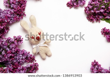 Lilac flowers with knitting toy rabbit on white background. Top view, flat lay, copy space.