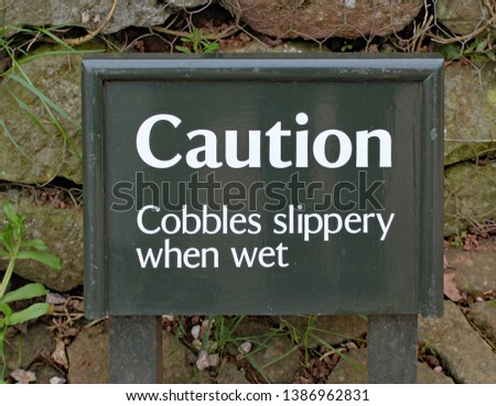 Brown wooden sign with the wording of Caution, Cobbles slippery when wet.