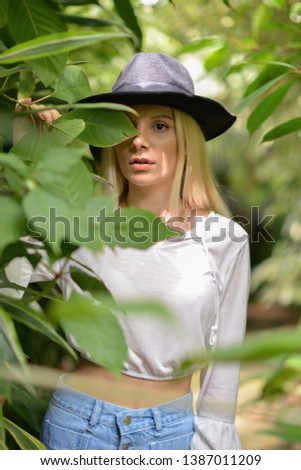 portrait of beautiful blonde girl with black hat, white blouse and jean shorts in the botanic garden