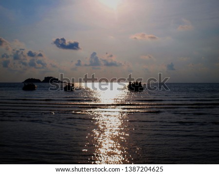 Golden light reflected on the sea at sunset Intersect with the silhouette of the ripples and boats, along with the gray-black clouds on the bright blue, naturally beautiful for background and texture.